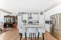 This kitchen features a central island with a granite countertop, white cabinetry, stainless steel appliances, and light-colored hardwood flooring - 