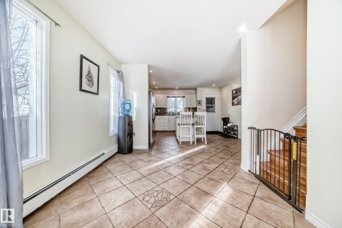 The property features tiled flooring, light-colored walls, and a view into the kitchen area with white cabinetry and an island - 16232 100 Street, Edmonton, AB - Indoor Photo Showing Other Room
