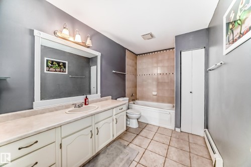 Bathroom featuring a vanity with a large mirror and an integrated sink, a tiled bathtub and shower area, and tiled flooring - 16232 100 Street, Edmonton, AB - Indoor Photo Showing Bathroom