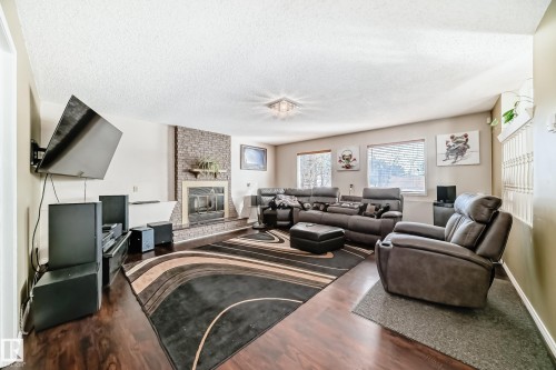 The living area features a stone fireplace, dark wood flooring, and a decorative area rug - 16232 100 Street, Edmonton, AB - Indoor Photo Showing Living Room With Fireplace