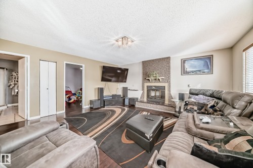 The living room features dark hardwood floors, a brick-accented fireplace, and neutral-toned walls - 16232 100 Street, Edmonton, AB - Indoor Photo Showing Living Room With Fireplace