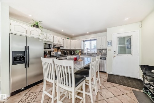 The kitchen features white cabinetry, stainless steel appliances, a large center island with seating, and tiled flooring - 16232 100 Street, Edmonton, AB - Indoor