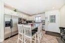 The kitchen features white cabinetry, stainless steel appliances, a large center island with seating, and tiled flooring - 16232 100 Street, Edmonton, AB  - Indoor 