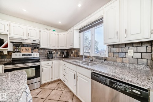 The kitchen features white cabinetry, granite countertops, a stainless steel oven and dishwasher, and a double basin sink beneath a window - 16232 100 Street, Edmonton, AB - Indoor Photo Showing Kitchen With Double Sink