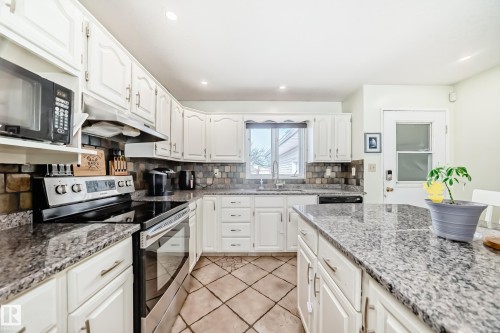 The kitchen features white cabinetry, granite countertops, a tile backsplash, and a large central island - 16232 100 Street, Edmonton, AB - Indoor Photo Showing Kitchen With Upgraded Kitchen
