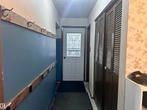 Entryway featuring a white front door with decorative glass inserts, a slatted ceiling, and wall-mounted coat hooks on a blue accent wall - 9915 95 Street, Westlock, AB - Indoor Photo Showing Other Room