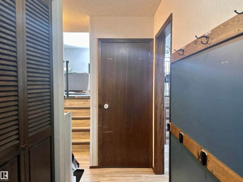 A hallway featuring a dark wood door, light-colored walls, and wooden stairs - 9915 95 Street, Westlock, AB - Indoor Photo Showing Other Room