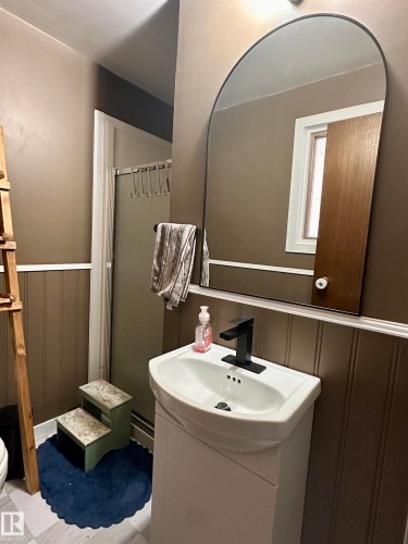 Bathroom featuring a white ceramic sink with a black faucet, a white vanity, and a large arched mirror - 9915 95 Street, Westlock, AB - Indoor Photo Showing Bathroom