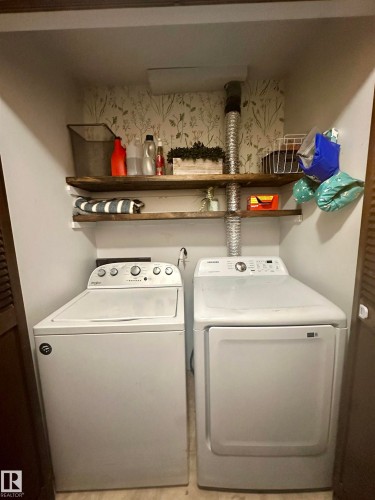 Dedicated laundry area featuring a washer and dryer, wood shelving, and a decorative botanical wallpaper accent - 9915 95 Street, Westlock, AB - Indoor Photo Showing Laundry Room