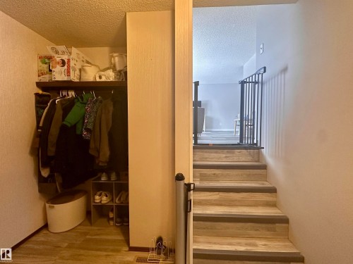 Entryway featuring wood-look flooring, a coat closet with shelving, and a stairway with black railings - 9915 95 Street, Westlock, AB - Indoor Photo Showing Other Room