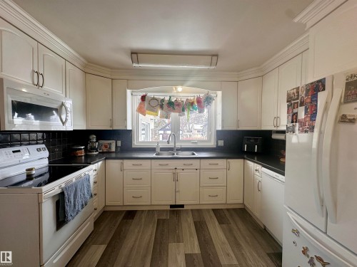 The kitchen features white cabinetry, dark countertops, and modern flooring - 9915 95 Street, Westlock, AB - Indoor Photo Showing Kitchen With Double Sink