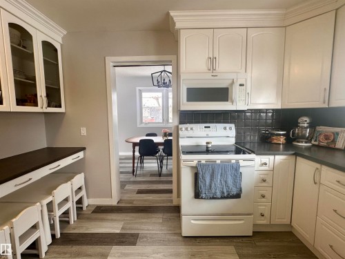 The kitchen features white cabinetry with crown molding, a white microwave, and a white electric range - 9915 95 Street, Westlock, AB - Indoor Photo Showing Kitchen