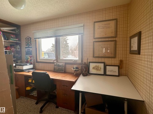 This room features a window providing natural light, a built-in wooden desk, and a textured ceiling - 9915 95 Street, Westlock, AB - Indoor Photo Showing Office