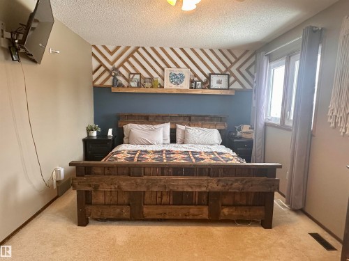 The room features a decorative wooden accent wall and a window with curtains - 9915 95 Street, Westlock, AB - Indoor Photo Showing Bedroom