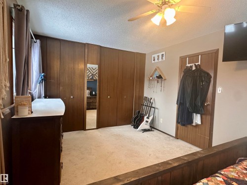 The property features carpeted flooring, a ceiling fan with integrated lighting, and wood paneling on the walls - 9915 95 Street, Westlock, AB - Indoor Photo Showing Bedroom