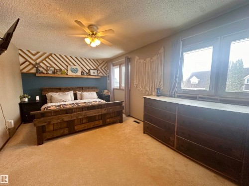 This bedroom features light-colored carpeting, a ceiling fan with integrated lighting, and multiple windows providing natural light - 9915 95 Street, Westlock, AB - Indoor Photo Showing Bedroom