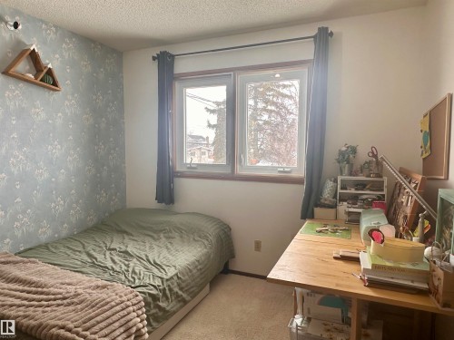 The room features a window providing natural light, a wall with floral-patterned wallpaper, and carpeting - 9915 95 Street, Westlock, AB - Indoor Photo Showing Bedroom