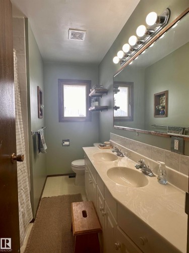 Bathroom featuring a double vanity with two sinks, a window providing natural light, and a toilet - 9915 95 Street, Westlock, AB - Indoor Photo Showing Bathroom