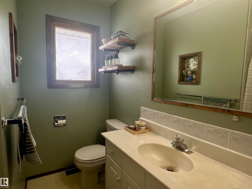 Bathroom with a vanity featuring an integrated sink, a large mirror with a wooden frame, and a window with a wooden frame - 9915 95 Street, Westlock, AB - Indoor Photo Showing Bathroom