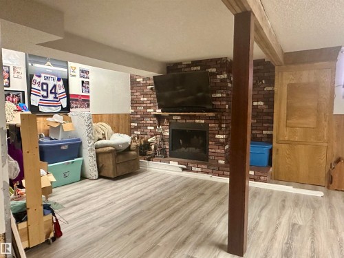 The property features a spacious room with light-toned flooring, a brick-clad fireplace, and wood paneling along the lower walls - 9915 95 Street, Westlock, AB - Indoor With Fireplace