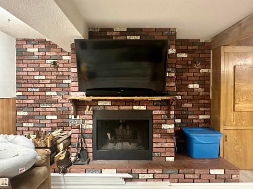 This living area features a brick fireplace with a mantle and hearth - 9915 95 Street, Westlock, AB - Indoor Photo Showing Living Room With Fireplace