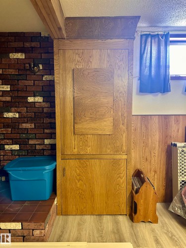 This space features a built-in wooden cabinet, brick wall details, and light-colored flooring - 9915 95 Street, Westlock, AB - Indoor Photo Showing Other Room