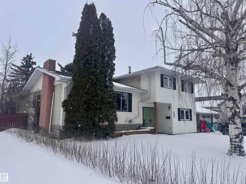 This property features a two-story exterior with white siding and dark-shuttered windows, complemented by a prominent brick chimney - 9915 95 Street, Westlock, AB - Outdoor