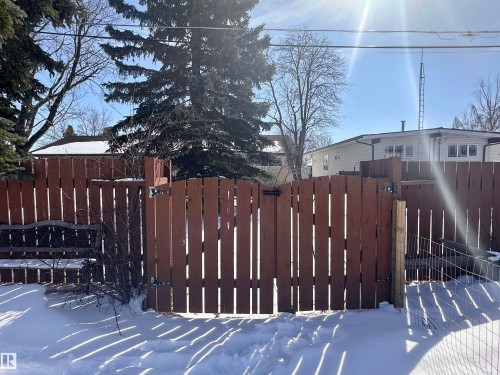 The property features a brown privacy fence with a gate, surrounded by snow-covered ground - 9915 95 Street, Westlock, AB - Outdoor