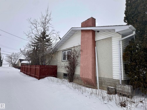 The property features a white exterior with a brick chimney and a red fence - 9915 95 Street, Westlock, AB - Outdoor With Exterior