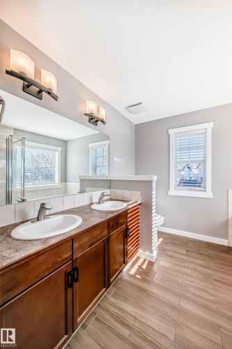 This bathroom features a double vanity with two sinks and undermount cabinetry, a large mirror, and tiled flooring - 6303 2 Avenue, Edmonton, AB - Indoor Photo Showing Bathroom