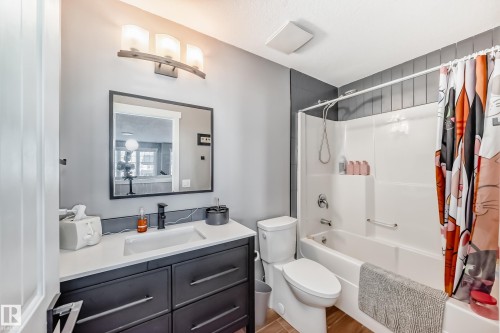 The bathroom features a modern vanity with a white countertop and dark cabinetry, a white toilet, and a bathtub with a shower - 6303 2 Avenue, Edmonton, AB - Indoor Photo Showing Bathroom
