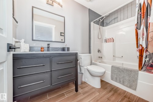 The bathroom features a vanity with a white countertop and a dark cabinet, a mirror, and wood-look flooring - 6303 2 Avenue, Edmonton, AB - Indoor Photo Showing Bathroom