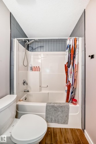 Bathroom featuring a white toilet, a shower-over-bath with a white surround, and wood-look flooring - 6303 2 Avenue, Edmonton, AB - Indoor Photo Showing Bathroom