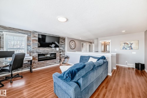 Living area featuring wood-look flooring, a fireplace with a decorative stone surround, and light gray walls - 6303 2 Avenue, Edmonton, AB - Indoor Photo Showing Living Room With Fireplace