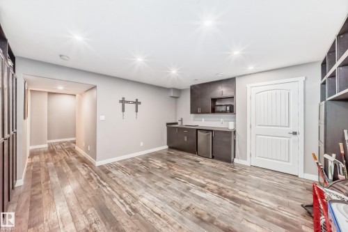 Spacious room featuring wood-style flooring, recessed lighting, a built-in wet bar with stainless steel appliances, and a white paneled door - 6303 2 Avenue, Edmonton, AB - Indoor