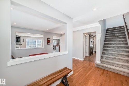 The property features hardwood flooring in the entry, a carpeted staircase with a dark wood handrail, and a pass-through window looking into a room with a large window - 6303 2 Avenue, Edmonton, AB - Indoor Photo Showing Other Room