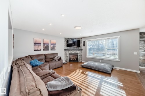 Living room featuring hardwood floors, a corner fireplace with stone surround, and windows providing natural light - 6303 2 Avenue, Edmonton, AB - Indoor Photo Showing Living Room With Fireplace