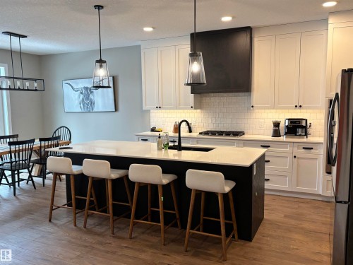 The kitchen features a large island with seating, white shaker cabinets, and a gas range with a dark range hood - 137 Graybriar Drive, Stony Plain, AB - Indoor Photo Showing Kitchen With Stainless Steel Kitchen With Upgraded Kitchen