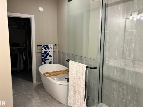 Bathroom featuring a freestanding white soaking tub, a glass-enclosed shower, and light gray tiled flooring and walls - 137 Graybriar Drive, Stony Plain, AB - Indoor Photo Showing Bathroom