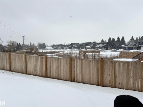 The property features a fenced yard with a clear view of the surrounding neighbourhood, including residential homes and evergreen trees in the distance - 137 Graybriar Drive, Stony Plain, AB - Outdoor