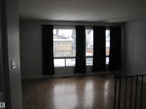 This room features large windows with dark curtains, warm-toned wood flooring, and light-colored walls - 3617 43A Avenue, Edmonton, AB - Indoor Photo Showing Other Room