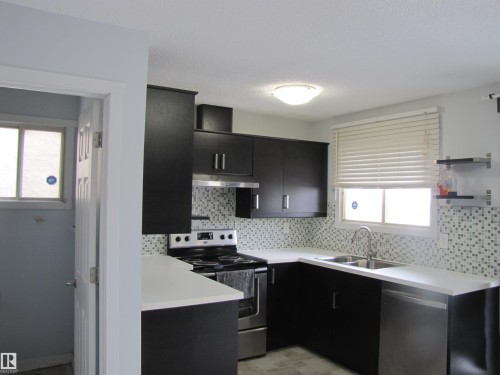 The kitchen features dark cabinetry, light countertops, a mosaic tile backsplash, and stainless steel appliances including a range and dishwasher - 3617 43A Avenue, Edmonton, AB - Indoor Photo Showing Kitchen With Stainless Steel Kitchen With Double Sink With Upgraded Kitchen