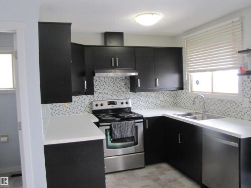 The kitchen features dark cabinetry with silver handles, white countertops, and a mosaic tile backsplash - 3617 43A Avenue, Edmonton, AB - Indoor Photo Showing Kitchen With Stainless Steel Kitchen With Double Sink With Upgraded Kitchen
