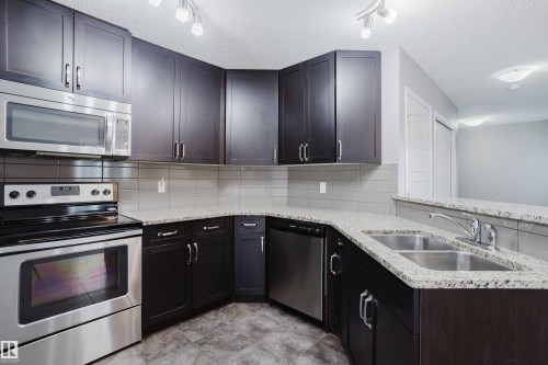 Well-appointed kitchen featuring dark wood cabinetry, stainless steel appliances, granite countertops, and a double basin sink - 14007 164 Avenue, Edmonton, AB - Indoor Photo Showing Kitchen With Double Sink