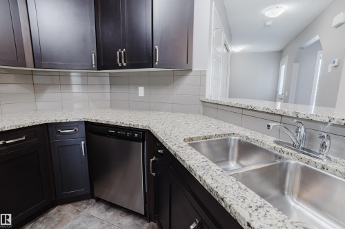 The kitchen features dark wood cabinetry, granite countertops, a stainless steel double sink, and a stainless steel dishwasher - 14007 164 Avenue, Edmonton, AB - Indoor Photo Showing Kitchen With Double Sink