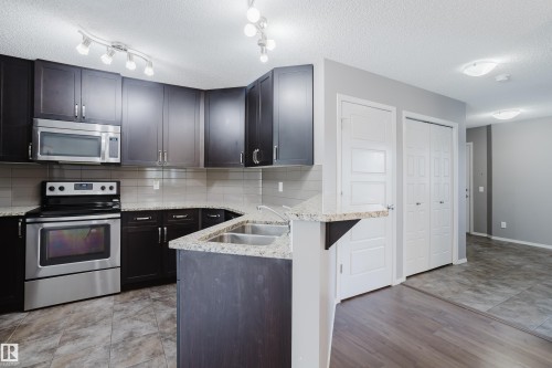 The kitchen features dark wood cabinetry, granite countertops, and stainless steel appliances including a range and microwave - 14007 164 Avenue, Edmonton, AB - Indoor Photo Showing Kitchen With Double Sink With Upgraded Kitchen