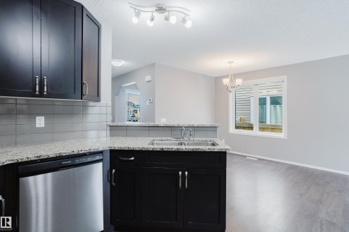 The kitchen features dark cabinetry, light-colored granite countertops, and a stainless steel dishwasher - 14007 164 Avenue, Edmonton, AB - Indoor Photo Showing Kitchen With Double Sink