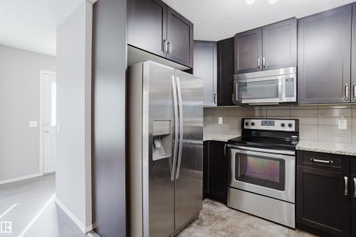 The kitchen features dark wood cabinetry, granite countertops, and stainless steel appliances including a refrigerator, range, and microwave - 14007 164 Avenue, Edmonton, AB - Indoor Photo Showing Kitchen With Upgraded Kitchen