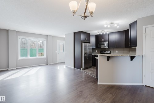 Open concept living space featuring wood-look flooring, a kitchen with dark cabinetry, stainless steel appliances, and a breakfast bar with a granite-look countertop - 14007 164 Avenue, Edmonton, AB - Indoor Photo Showing Kitchen