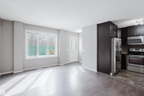 The property features a bright open concept living area with large windows, durable flooring, and a kitchen equipped with dark cabinetry and stainless steel appliances - 14007 164 Avenue, Edmonton, AB - Indoor Photo Showing Kitchen